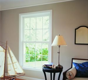 Living room with a model boat, table and lamp, mirror, couch, and a double-hung window looking out to the yard